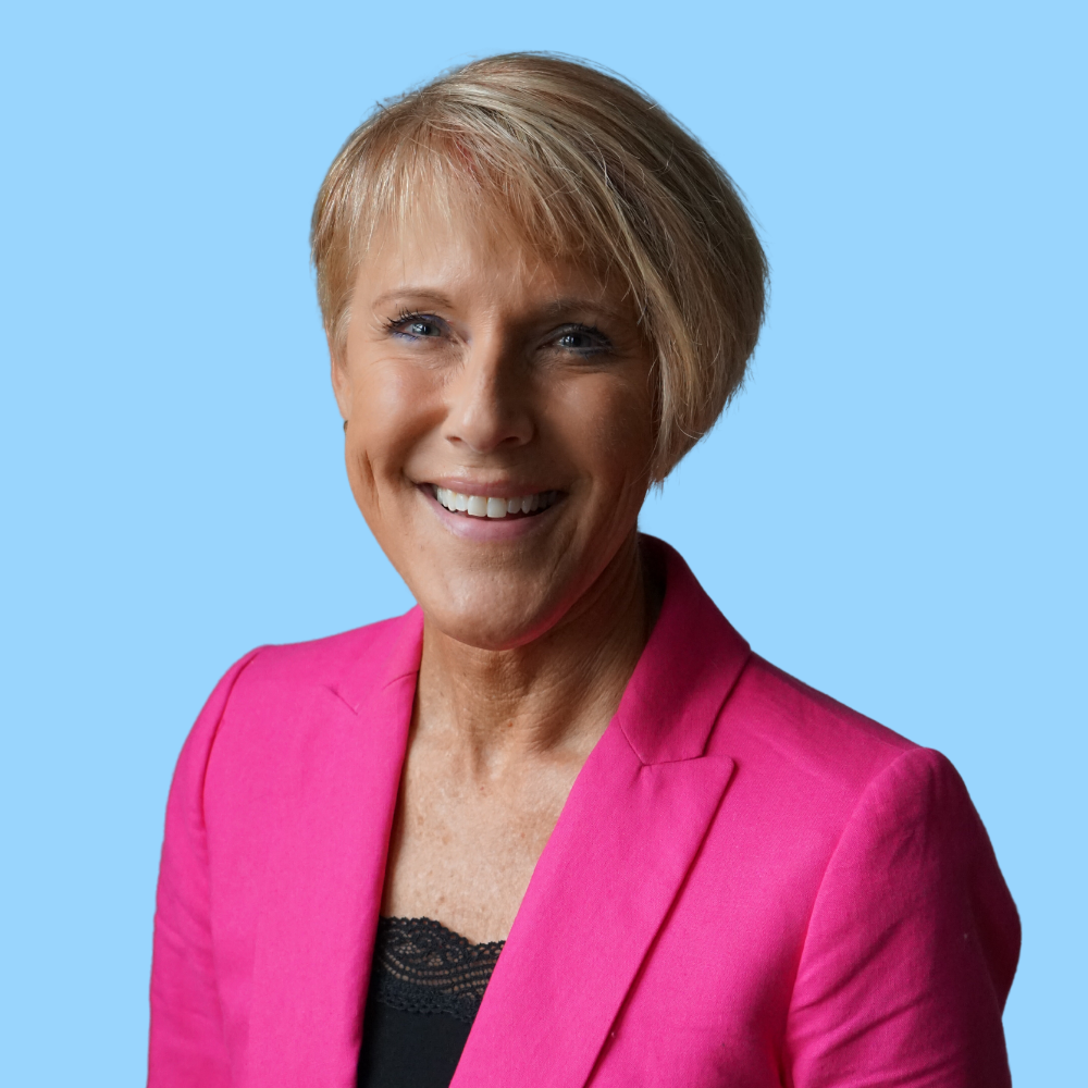 headshot of woman in pink jacket on blue background