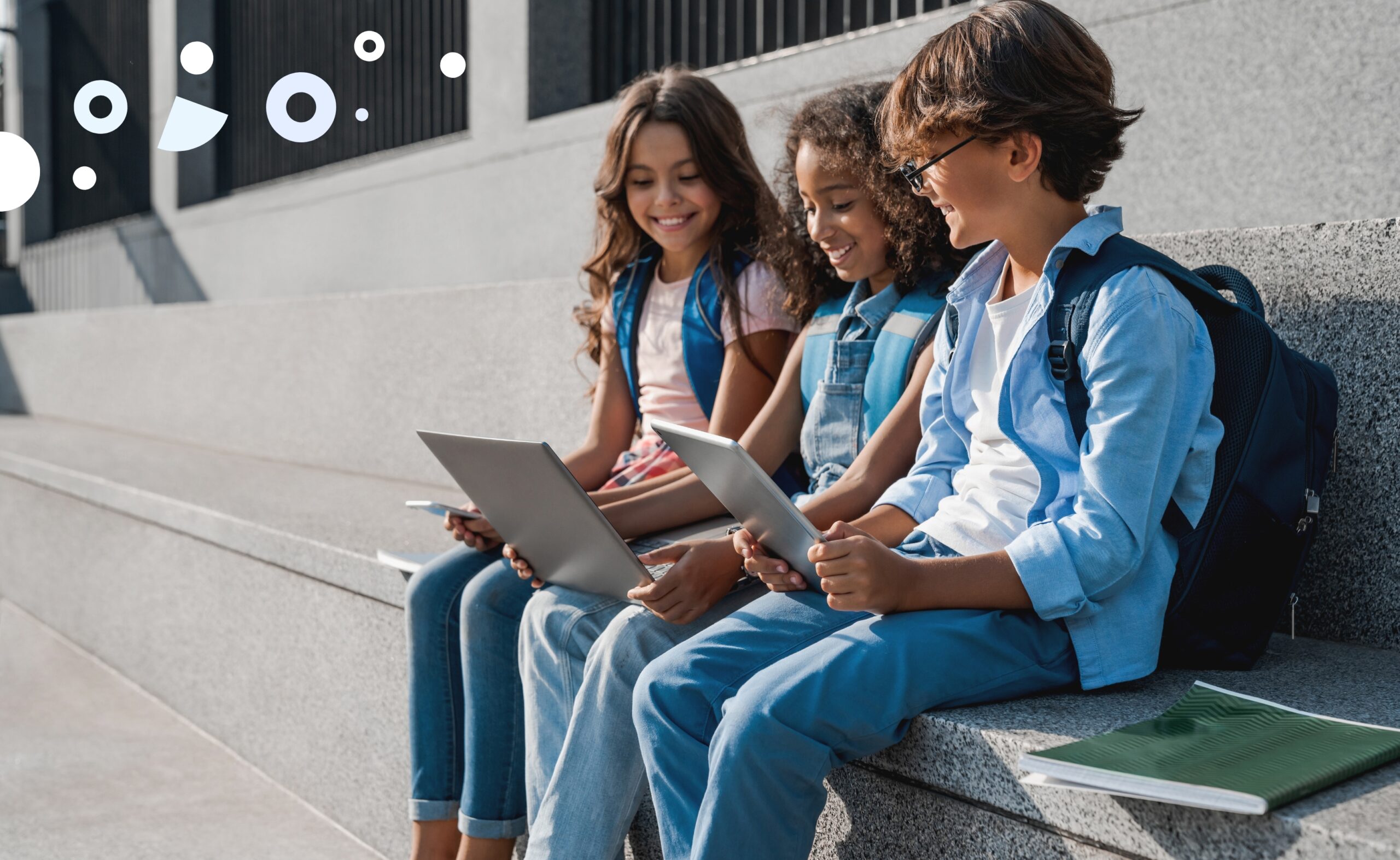 three students sitting on ledge with laptops and backpacks